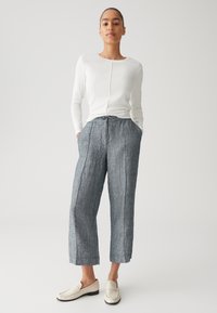 Witte lange mouw top met een ronde hals, gecombineerd met losse grijze linnenblend cropped broek met voorkruisen. Witte instapschoenen.