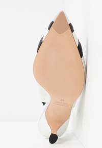 Chaussure à talon haut pour femme à bout pointu avec semelle lisse couleur tabac, embout du talon noir, et tige blanche avec des accents noirs, taille 37 indiquée sur la semelle.