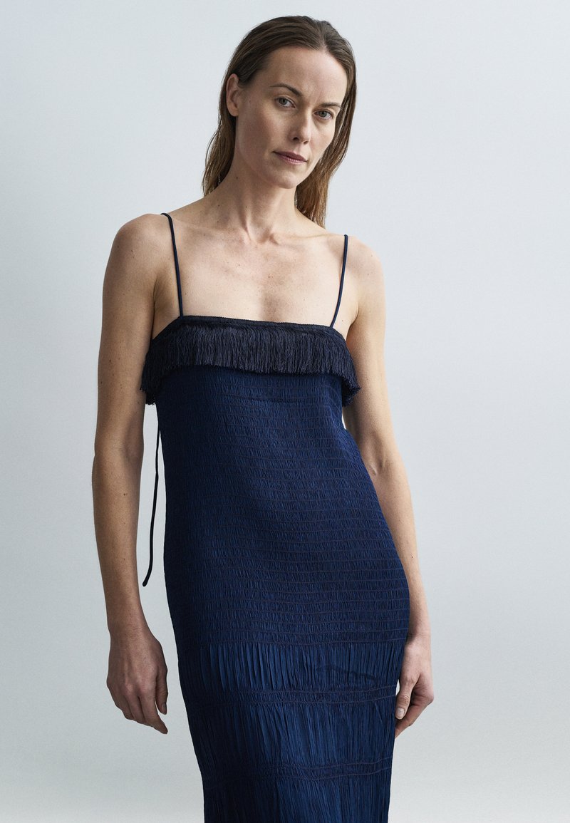 Tengerészkék ruha bonyolult smock díszítéssel, rojtos felsőrésszel. Vékony pántok és karcsú sziluett. Minimalista kialakítás.