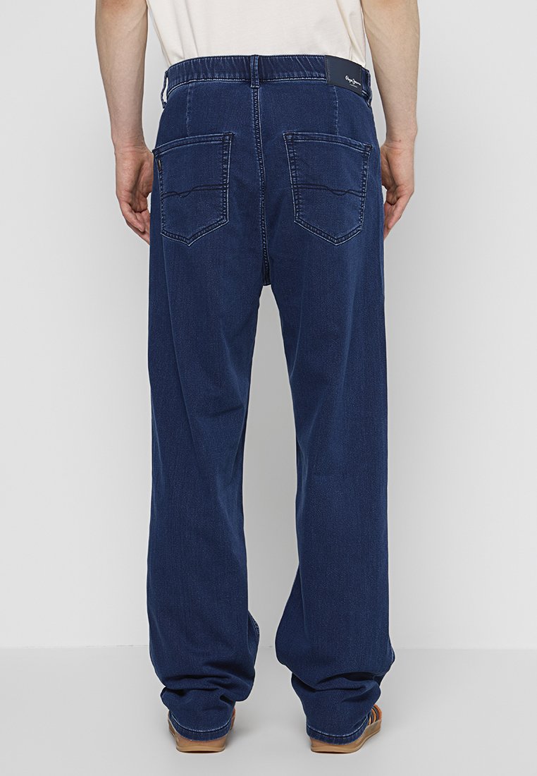 Jeans en denim bleu foncé, à coupe droite et ample, avec deux poches arrière et une étiquette à la taille. Détails de couture simples.