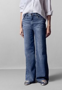 Vaqueros de pierna ancha color azul claro, confeccionados en denim, con un diseño clásico de cinco bolsillos, cierre frontal de botón y un sutil detalle de desvanecimiento.