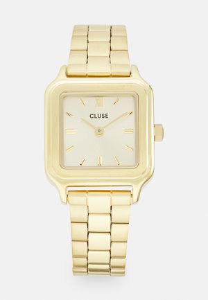 Gold square watch with a yellow gold metal bracelet. Cream-colored dial features gold hour markers, brand name “CLUSE,” and a crown.
