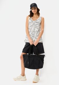 Czarna torba na ramię z płótna, z regulowanymi paskami, zamykanymi kieszeniami i subtelną teksturą, zestawiona z pasującą bluzką bez rękawów w paski i ciemnymi szortami.