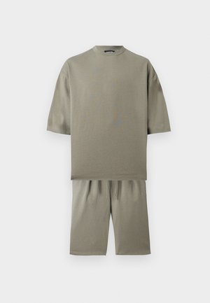 Beige oversized T-shirt met korte mouwen gecombineerd met beige shorts tot op de knie, afgebeeld op een witte achtergrond.