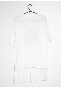 T-shirt bianco oversize, maniche corte, scollatura rotonda, tessuto leggero, orlo asimmetrico con spacco laterale, design minimalista.