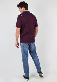 Polo shirt violet foncé avec un col marine, à manches courtes, associé à un jean bleu clair et des baskets noires, vu de dos.