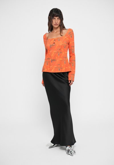 Oranžna dolgosleeve majica s cvetličnim vzorcem in kvadratnim dekoltejem, v kombinaciji s sleek črno satensko krilo in metalik špicastimi čevlji.