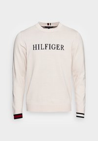 Cremfarbener Strickpullover mit Rundhalsausschnitt, der "HILFIGER" in Marineblau zeigt. Mit marineblauen, weißen und roten Streifen an den Bündchen akzentuiert.