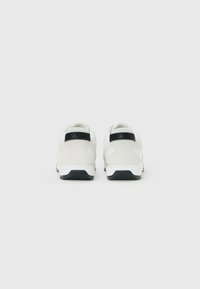 Een paar witte sneakers met zwarte zoolaccenten, gezien vanaf de achterkant op een effen witte achtergrond.