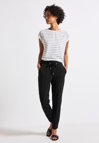 Vit randig t-shirt med kort ärm, kombinerad med svarta smala byxor med snörning i midjan och sidofickor. Svarta sandaler fulländar outfiten.