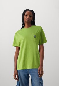 Svetlo zelena majica s kratkimi rokavi iz bombaža s krožnim izrezom in žepom na levi strani prsnega dela, ki ima mornarsko modro oznako.