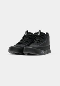 Chaussures montantes noires en tissu texturé, avec un collier rembourré, un empiècement renforcé à l'avant, et une semelle en caoutchouc durable présentant un détail de logo sur le côté.