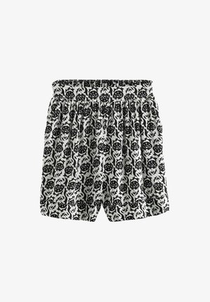 Schwarz-weiße gemusterte Shorts mit einem elastischen Bund und geraffter Textur, die ein Blumen- und Gesichtsmotiv durchgehend aufweisen.
