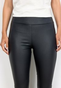 Leggings neri in ecopelle con una texture liscia, vita alta e un design aderente, che mette in evidenza una forma contornata.
