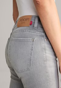 Szürke farmernadrág, bőr derékpánt címkével, rajta a "JOOP! JEANS" felirattal. Két hátsó zseb, ezüst színű szegecsekkel.