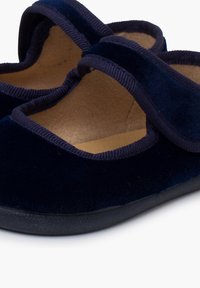 Zapatos de terciopelo azul marino con forma redondeada, que cuentan con dos correas de tela en la parte superior y un forro interior suave. Suelas de goma negra.