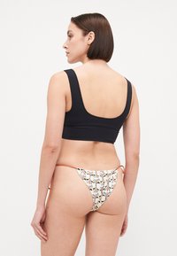 Haut de bikini noir cropped associé à un bas de bikini multicolore à motifs avec des liens sur les côtés et une texture lisse.