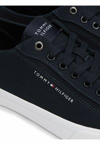 Primer plano de una zapatilla Tommy Hilfiger de color azul marino con suela blanca, cordones negros y el logo de la marca en el costado y en la lengua.