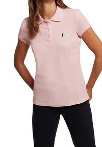 Polo rose clair avec un col classique, une patte à trois boutons et un petit logo bleu marine sur la poitrine gauche. Texture douce et lisse.