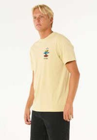 Lichtgele katoenen t-shirt met een ronde halslijn en korte mouwen. Heeft een kleurrijk logo op de borst en een losse pasvorm.