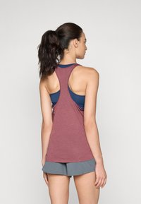 Vinröd idrottstopp med racerbackdesign, med en strukturerad tygkvalitet. Kombinerad med grå shorts, som visar lager av underkläder i marinblått.