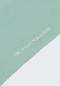 Lichtgroene stof met een gladde textuur, voorzien van witte stiksel en het "TOM TAILOR" logo in het wit gedrukt.