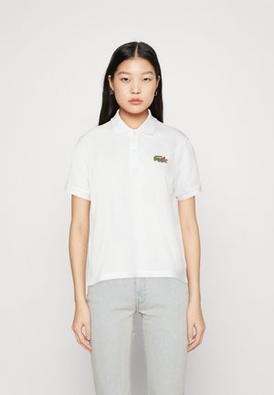 Camisa polo blanca con cuello clásico, mangas cortas y un logo bordado en verde en el pecho. Material de algodón suave, corte relajado.