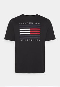Černé tričko s krátkým rukávem značky Tommy Hilfiger, s červenými, bílými a námořnickými pruhy a textem "TOMMY HILFIGER EST. MCMLXXXV" na přední straně.
