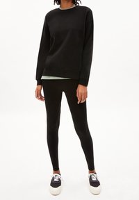 Czarny sweatshirt z długimi rękawami i okrągłym dekoltem, w połączeniu z czarnymi legginsami i ciemnymi trampkami z białą podeszwą. Gładka tekstura.