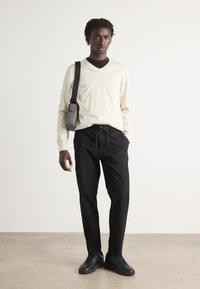 Lichtbeige langemouw V-hals trui, zwarte joggingbroek met koord, en zwarte sneakers. Minimalistisch ontwerp met een casual pasvorm.