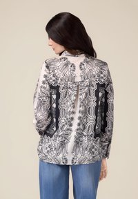Blouse à manches longues en tissu léger présentant un motif paisley noir et blanc, avec un détail plis à l'arrière. Finie par un col rond.