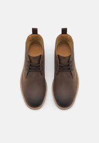 Botas chukka de cuero marrón con un acabado suave, punta redonda y acentos en color beige. Cuentan con cordones y una tira en la parte posterior para facilitar su uso.