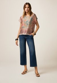 Bloemendessine doorschijnende blouse in tinten roze en blauw, gecombineerd met brede donkere denim jeans en zwarte sandaaltjes met banden.