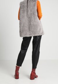 Gilet in pelliccia sintetica grigia, camicia arancione a maniche lunghe, pantaloni in pelle nera e stivaletti rossi con stampa a serpente e tacco largo.