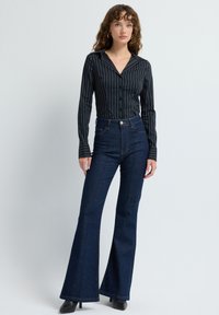 Černá pruhovaná košile na knoflíky s dlouhými rukávy a tmavě modré kalhoty s vysokým pasem a rozšířenými nohavicemi. Hladká látka s výraznými švy a odvážnou siluetou.