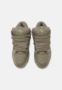 Olivzaļas kedas ar teksturētu auduma virsmu un gludu gumijas zolīti. Tās ir aprīkotas ar izteiktiem šņorēm, reljefa logotipu un polsterētu apkakli.