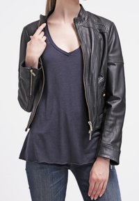 Černá kožená bunda na zip s vysokým límcem a švy, nošená přes námořnickou modrou tričko s výstřihem do V.