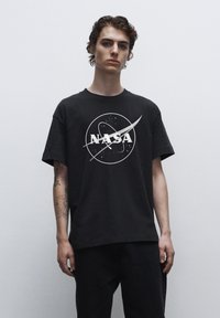 Černé bavlněné tričko s bílým logem NASA a grafikou obíhajících planet, krátké rukávy a volný střih.