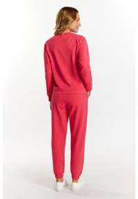 Różowa bluza i dopasowany zestaw dresowy, prezentujące luźny krój, ściągacze u rękawów i w pasie, pokazane z tyłu. Widoczne białe sneakersy.