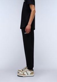 Black T-shirt, black sweatpants, and beige and white sneakers with black accents. The outfit features simple design elements and textures.