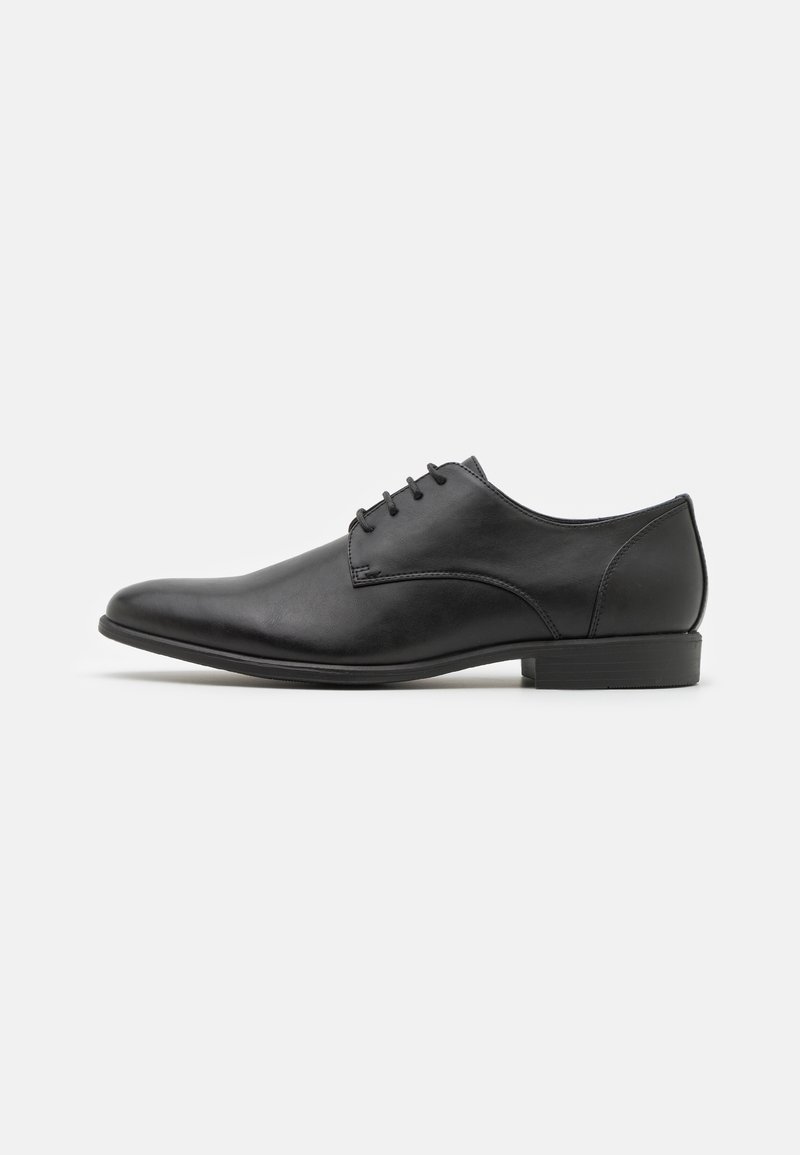 Chaussure Oxford formelle pour hommes en cuir noir avec laçage fermé et petit talon empilé, vue de profil.