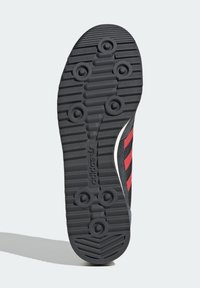 Suela negra de una zapatilla deportiva con un patrón texturizado, que presenta tres franjas rojas y un acento blanco a lo largo del costado.