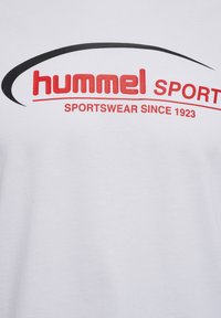 T-shirt en coton blanc arborant un logo "hummel" rouge et le texte "SPORTSWEAR SINCE 1923", souligné par une ligne courbe noire au-dessus du logo.