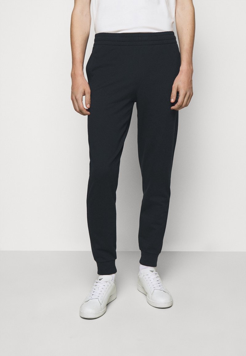 Pantalons de jogging bleu marine en tissu doux, avec une taille élastique et des jambes fuselées, portés avec des baskets blanches.