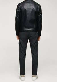 Giacca in pelle nera con spalle texture abbinata a pantaloni cargo grigi, dotati di tasche laterali, e sneakers bianche.