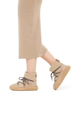 Beige ankelstøvler med furfór, struktureret stof og grå snørebånd. Har en tyk gummisål og syede detaljer for holdbarhed.
