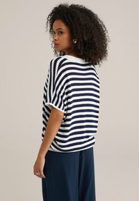 Tumedate ja valged triibulised lühikeste varrukatega pluusid, lõdva lõikega, tekstuurse kudumisega kangas ja ümmargune kaelus. Koos tumedate pükstega.