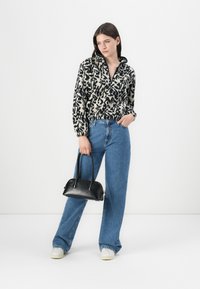 Pullover a fantasia bianca e nera con colletto alto, abbinato a jeans a gamba larga blu e una piccola borsa nera. Dettagli di tessuto strutturato visibili.