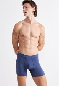 Miestne námornícké modré boxerky SLOGGI, elastická tkanina, priliehavý dizajn, hladká štruktúra, široký pás s logom, dĺžka po polovicu stehna.