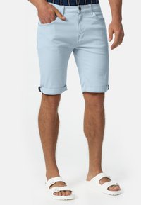 Svijetloplave pamučne kratke hlače sa zavrnutim rubovima, s prednjim džepovima i uskim krojem, u kombinaciji s bijelim sandalama.